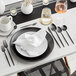 A table set with a white plate, Acopa Odin stainless steel fork, and silverware.