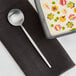An Acopa brushed stainless steel bouillon spoon in a bowl of soup on a table.
