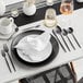 A black Odin stainless steel teaspoon on a white table with a plate and silverware.