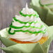 A cupcake with white frosting and green swirls made with Satin Ice Green Vanilla Glitter Glaze.