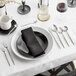 A table set with Acopa Odin brushed stainless steel oyster forks, silverware, and a black napkin.