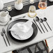 A black table setting with a spoon on a white plate.