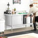 A man in a brown apron preparing food on a Steelton stainless steel table with sliding doors.