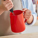 A person pouring milk into a red Acopa frothing pitcher.