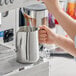 A person pouring milk into a silver Estella Caffe frothing pitcher.