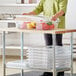 A person standing next to a table with Vigor clear polycarbonate food storage containers and lids.