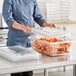 A woman in a chef's uniform opening a Vigor clear polycarbonate food storage container filled with carrots.