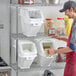 A man in an apron putting food into a white plastic container with a clear window.