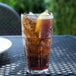 A Bahama clear plastic tumbler filled with brown liquid, ice, and lemon slices on a table.