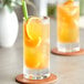A glass of Tractor Beverage Co. Clementine juice with a straw and an orange slice on a table.