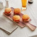 An Acopa faux wood melamine serving board with burgers on it.