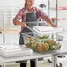 A woman in an apron using a Cambro food storage container to store pineapples.