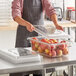 A woman in an apron using a Cambro clear polycarbonate food storage container to store red apples.