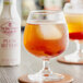 A glass of liquid with ice and Fee Brothers Plum Bitters on a table.