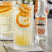 A glass of liquid with orange slices and a bottle of Fee Brothers Orange Flower Water on a table in a cocktail bar.