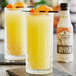 A bottle of Fee Brothers Gin Barrel Aged Orange Bitters on a table with two glasses of orange juice and a bottle of liquor.