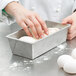 A person's hand kneading dough in a Chicago Metallic bread loaf pan.