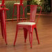 A Lancaster Table & Seating red metal chair with white cushion in a restaurant.