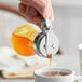 A person using a Choice glass teardrop syrup dispenser to pour syrup into a cup.