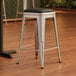 A Lancaster Table & Seating silver metal backless counter height stool with a black vinyl cushion.