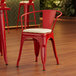A Lancaster Table & Seating red metal arm chair with white cushion in a restaurant.