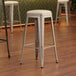 Lancaster Table & Seating silver metal backless barstools with white vinyl cushions.