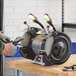 A man using a Genesis 8" bench grinder with lights and eye shields to cut wood.