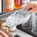 A person using a Choice aluminum scoop to pick up ice cubes.