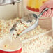 A hand using a Choice aluminum scoop to pour popcorn from a machine.