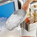 A person using a Choice aluminum ice scoop to pour ice into a bowl.