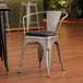 A Lancaster Table & Seating metal arm chair with black vinyl cushion.