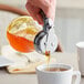 A hand pouring syrup from a Choice Glass Teardrop Syrup Dispenser into a cup of tea.