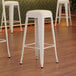 A group of Lancaster Table & Seating white backless barstools with white cushions.