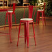 A red Lancaster Table & Seating cafe barstool with white cushion on a wooden floor.