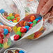 A person holding a Choice aluminum scoop of candy over a jar.