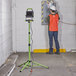A man wearing a vest and helmet standing next to a PowerSmith telescoping tripod with a work light on it.