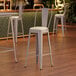 A Lancaster Table & Seating nickel gray barstool with a white cushion.