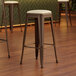 A close-up of a Lancaster Table & Seating copper backless bar stool with a white vinyl cushion.