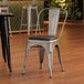 A Lancaster Table & Seating silver metal cafe chair with black vinyl cushion.
