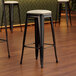 A close-up of a Lancaster Table & Seating black bar stool with a white cushion.