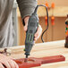 A person using a Genesis variable speed rotary tool to drill a piece of wood.