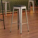 A set of three Lancaster Table & Seating silver metal backless bar stools with black cushions.