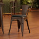 A Lancaster Table & Seating metal arm chair with a black cushion on the seat.