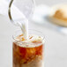 A glass of milk being poured into a glass of brown liquid.