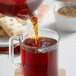 A person pouring Davidson's Organic Tulsi Mango Peach tea into a glass cup.