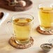 A glass mug of Davidson's Organic Peppermint Leaves tea on a wooden table with a strainer of herbs.