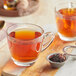 A glass mug of Davidson's Organic Rose Congou tea with a strainer and a spoon on a wooden surface.