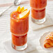 A glass of Davidson's Organic Mango Peach Iced Tea with ice and fruit on top on a table with a croissant.