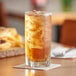 A glass of Brisk unsweetened iced tea with ice on a table next to a sandwich.