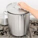 A person using a Vollrath stainless steel stock pot on a stove with a lid.